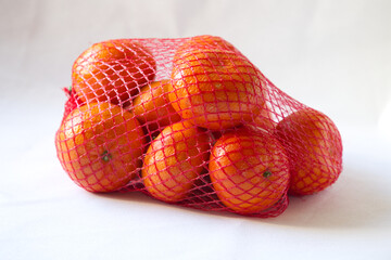 a group of tropical fruit orange mandarin, clementine, tangerine in a red mesh bag packing on white...