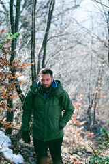 Attractive Caucasian male hiking in forest. Young hiker walking uphill through the mountain woods in late winter.