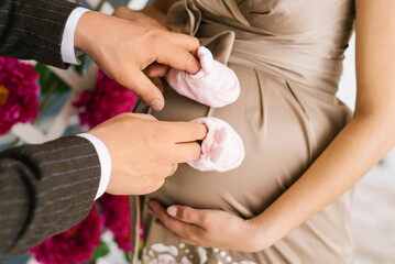 Male hands of a woman put on shoes for youth and hold them near the pregnant belly