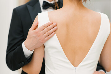 The groom gently and tenderly embraces the bride by the shoulders. Close-up of the hands of a happy couple