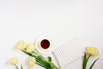 Spring yellow tulips, coffee mug, notebook on a white background. Flat position, top view.