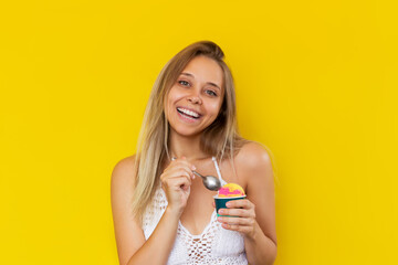 A young beautiful caucasian happy blonde woman smiles enjoying the taste of sorbet, holding a cream...