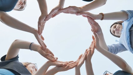 Friends make a circle with their palms against the blue sky.