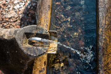 Old rustic drinking water fountain in the forest. Wooden construction, rusty metal pipe and faucet, streaming water. Close up shot, shallow depth of field, no people
