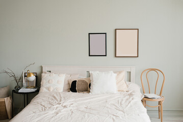 Double bed with white linens and beige pillows in a bright Scandinavian bedroom, mockup paintings above the bed