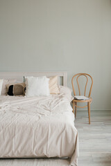 Fototapeta na wymiar Bedroom interior in Scandinavian style. A bed with beige linens and pillows and a chair by the bed
