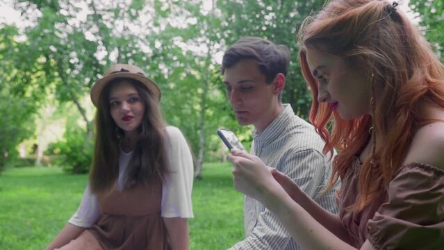 The girl shows her friends photos on the phone in nature in the summer
