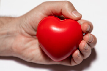 Selective focus on a red heart in a caucasian hand on a white background.  The hand is out of focus. 