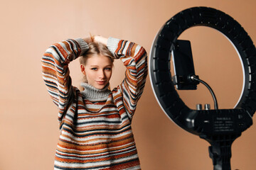 Beautiful young woman is fixing her hair and slightly smiling in front of the mobile camera. The girl is recording tutorials for the fashion blog. Concept of blogging
