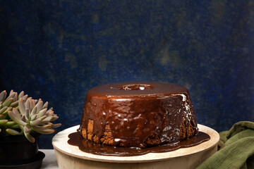 Homemade chocolate cake with syrup poured on top. Dark mottled blue background in the background. Space for art.