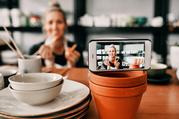 Art is too important not to share. Cropped shot of an attractive mature woman using her cellphone to record her pottery process for her blog.