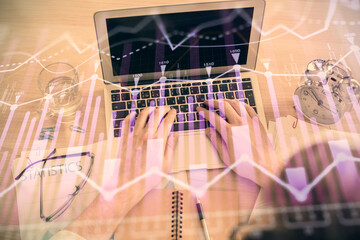 Double exposure of man's hands typing over laptop keyboard and forex chart hologram drawing. Top view. Financial markets concept.