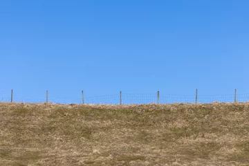 Foto op Plexiglas Fence on topp of grassy hill with clean blue sky background. © Andreas Bergerstedt