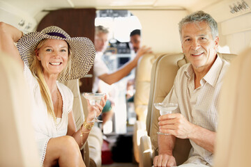Flying in style. Shot of a mature couple sitting in the back of a private jet drinking cocktails.