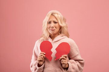 Unhappy lady holding two halves of cut paper heart and crying, feeling hurt, going through romantic...
