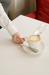 Fototapeta na wymiar Waiter hand holding a cup of capuccino coffee from a restaurant table