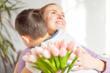 A cute son giving his mother a bouquet of tulips congratulating her on mother's day while...