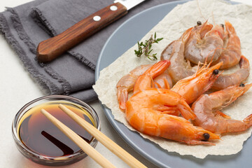 Shrimps on paper on gray plate. Soy sauce in glass bowl and chopsticks.