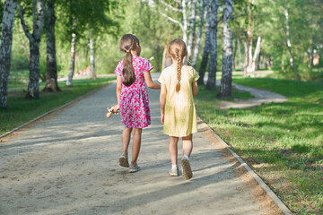 A photo from the back of two cute charming girls walking together along a path in the park. The concept of childhood love and friendship, best friends forever. High quality photo
