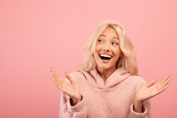 Excited stylish woman looking aside at free space, demonstrating space for your advertisement text on pink background