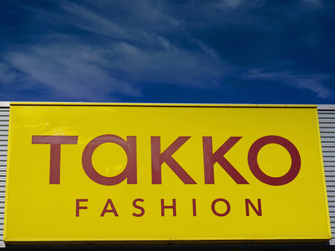 Gelbes Logo von Takko Fashion (deutsche Modekette) an einer Fassade vor  blauen Himmel