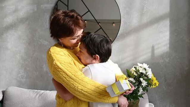 mother hugging her child son as holding gift and a bunch of flowers.mother's or women's day