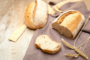 loaf of fresh bread and cutted slice of baguette bun on wooden rustic background with copy space, baked pastry food closeup