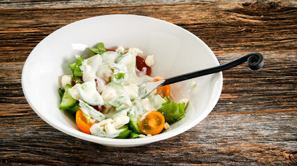 Vegetables salad with dressing inside white bowl on rustic table