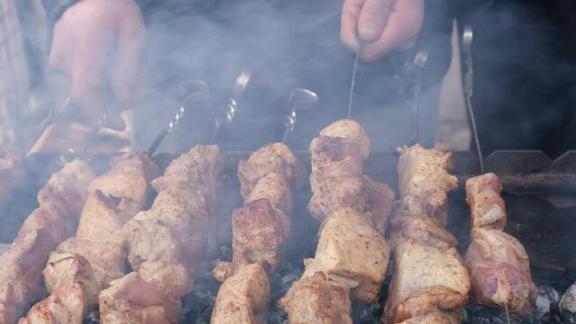 a man roasts meat on a fire. Close-up of hands and barbecue. Grilling pork neck. Roasted carrots. Fatty food, festive food of the CIS countries. May 1, working day. Non vegan food. Street food