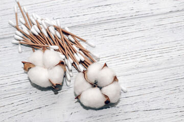 Cosmetic eco sticks on a cardboard base are scattered with cotton on a white background.