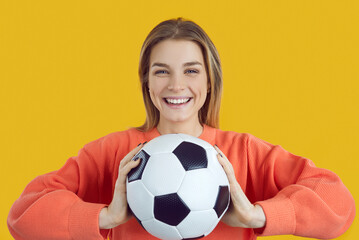 Pretty lady holding football on yellow background. Woman with soccer ball looking at camera and smiling. Beautiful girl having fun at World Cup competition. Happy pupil playing sports in PE class