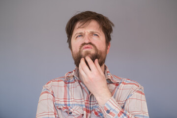 Pensive man with beard has clever expression, looks thoughtfully aside