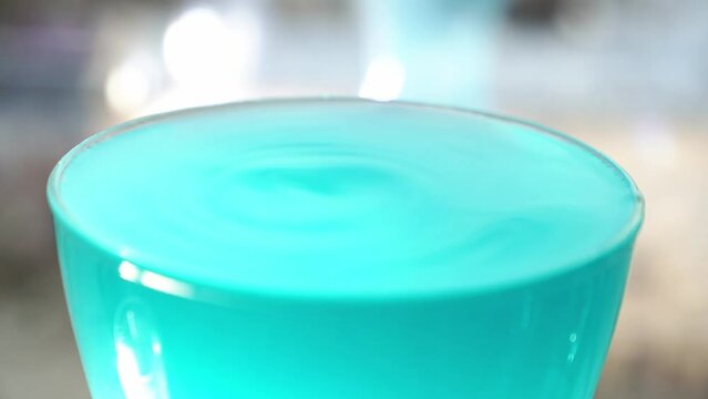 In slow motion, a jet of liquor pours into a glass with a drink and makes a splash on the surface. Alcoholic drink with blue curacao. High quality FullHD footage