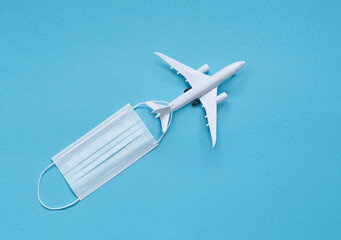 a white plane with a medical mask on a blue background. the concept of social distance. travel planning.