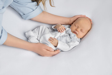 mom's hands hold newborn baby boy in a suit sleeping on a  light background. Happy pregnancy and childbirth. Children's theme. Top view