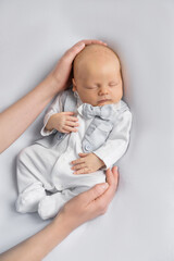 mom's hands hold newborn baby boy in a suit sleeping on a  light background. Happy pregnancy and childbirth. Children's theme. Top view