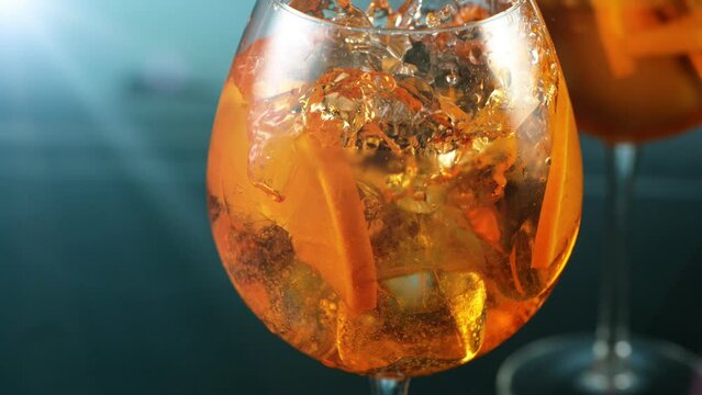 Super slow motion. Ice cube falling into glass of orange cocktail. Aperol spritz