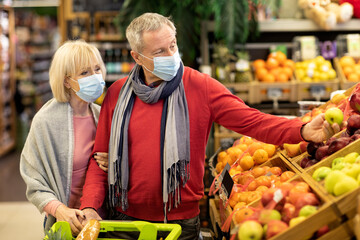 Elderly couple in face masks choosing fresh fruits