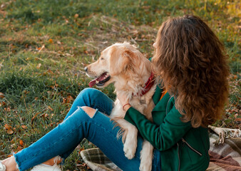 Portrait of a curly young woman hugging her golden retriever dog in the park. Young curly woman sitting with her dog in autumn leaves