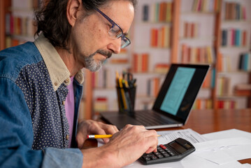 Male accountant in the office uses a calculator and writes data in a notebook. Profit analysis, taxes and payments calculations, preparation of financial statements concept