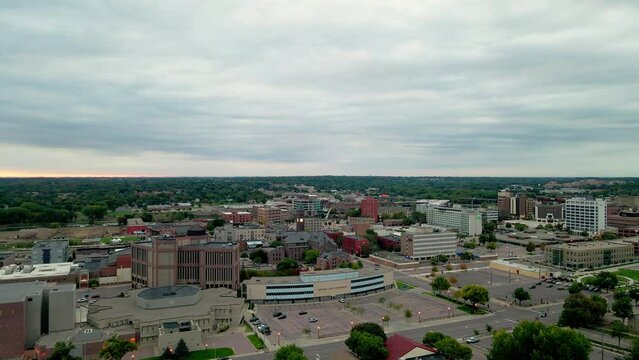 Aerial view of cityscape in Minnesota on a cloudy day. Mix of older and newer buildings, large and small, commercial buildings and church. Tree lined streets in the background. 