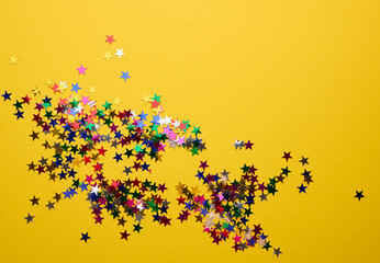 shiny multicolored star confetti scattered on a yellow background, festive backdrop for birthday,...