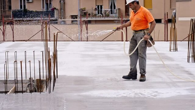 Worker moistens the surface of the concrete used for the construction of a floor