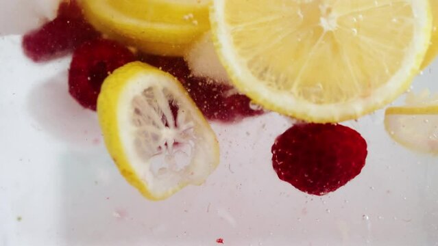 fresh raspberries and lemon slices falling into iced beverage