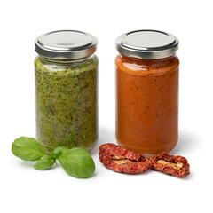 Glass jar with red and green Italian pesto with dried sweet tomatoes and fresh basil leaves in front  isolated on white background 