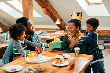 Happy African American woman has fun while family is surprising her with gift on Mother's day at home.