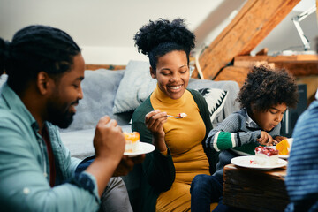 Happy African American woman enjoys in eating cake with her family at home.