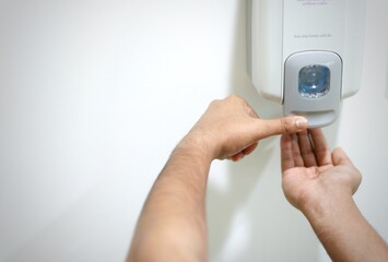 HANDS UNDER A MANUAL WALL MOUNTED SANITISER.