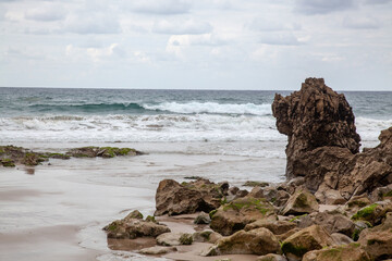 Fototapeta na wymiar Sandy beach among the rocks. Small waves on the sea. Cloudy sky.