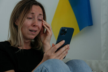 Young anxious woman with cried out eyes reading the news about Ukraine on her cellphone. Close up,...